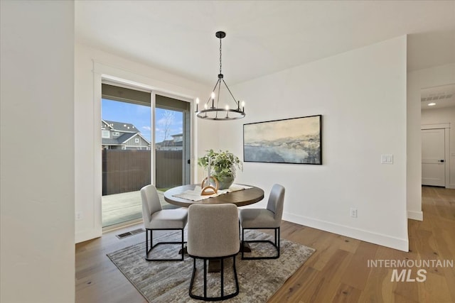 dining area with baseboards, wood finished floors, visible vents, and an inviting chandelier