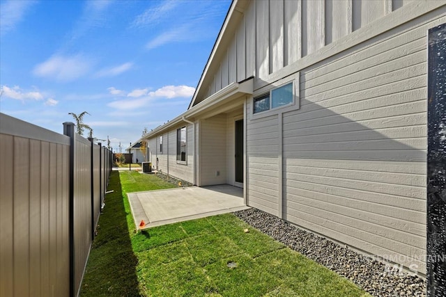 view of side of home with central air condition unit, a lawn, board and batten siding, a patio area, and a fenced backyard