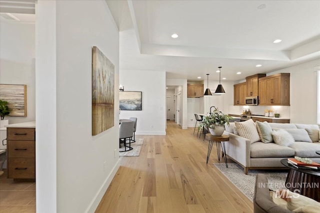 living area with recessed lighting, light wood-type flooring, a raised ceiling, and baseboards