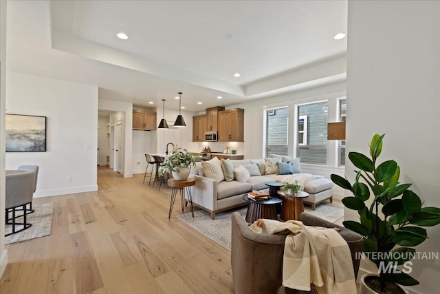 living room featuring light wood finished floors, baseboards, a raised ceiling, and recessed lighting