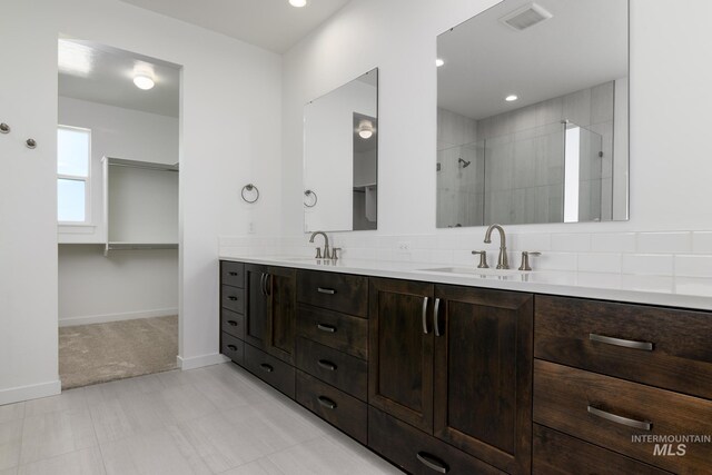 full bathroom with double vanity, visible vents, tiled shower, and a sink