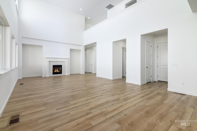 unfurnished living room featuring light hardwood / wood-style flooring, a towering ceiling, and a fireplace