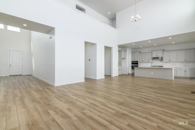 unfurnished living room with recessed lighting, a notable chandelier, a towering ceiling, baseboards, and light wood-type flooring