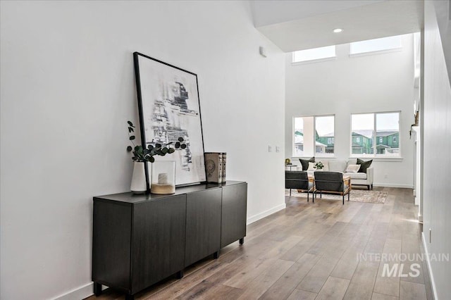 hall with baseboards, light wood-style floors, and a towering ceiling