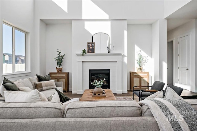 living room featuring a glass covered fireplace, baseboards, wood finished floors, and a towering ceiling