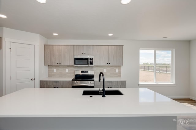 kitchen featuring sink, an island with sink, stainless steel appliances, and light hardwood / wood-style flooring