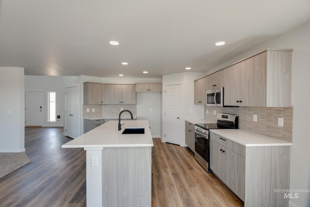 kitchen with sink, a kitchen island with sink, appliances with stainless steel finishes, and light hardwood / wood-style flooring