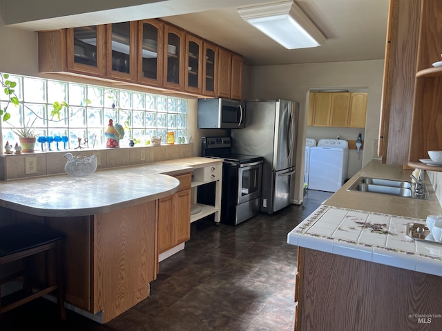 140 3rd St, Grand View, ID 83624 - kitchen with glass insert cabinets, brown cabinetry, a sink, stainless steel appliances, and washing machine and dryer
