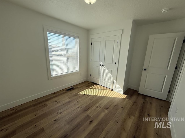 unfurnished bedroom with visible vents, baseboards, hardwood / wood-style floors, a closet, and a textured ceiling