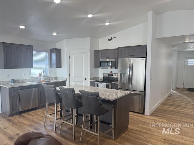 kitchen featuring a sink, stainless steel appliances, lofted ceiling, and light stone countertops