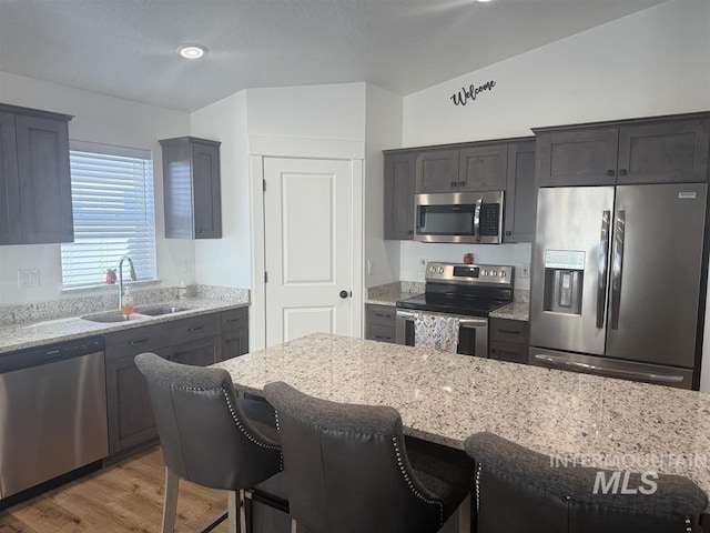 kitchen featuring a breakfast bar area, light stone countertops, appliances with stainless steel finishes, and a sink