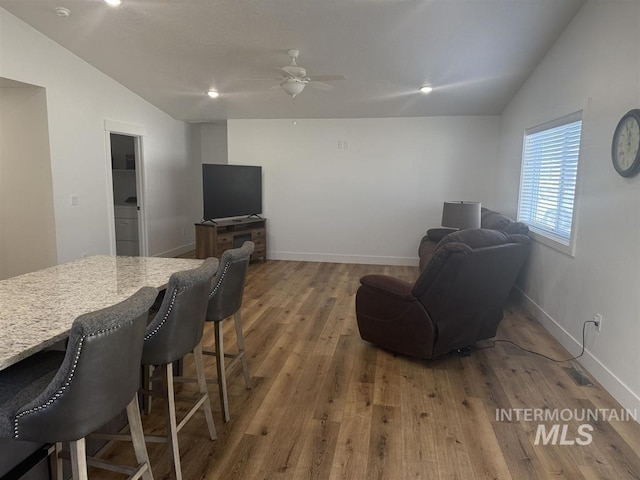 living room featuring wood finished floors, a ceiling fan, baseboards, and vaulted ceiling