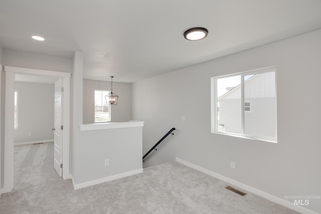 hallway with light colored carpet and an inviting chandelier