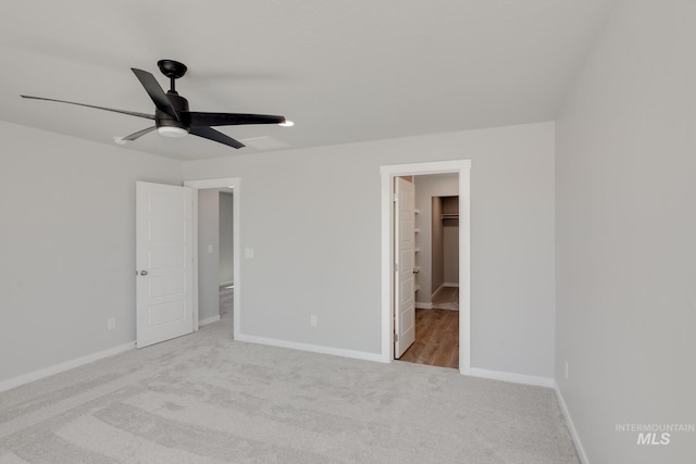 unfurnished bedroom featuring a closet, a spacious closet, ceiling fan, and light colored carpet