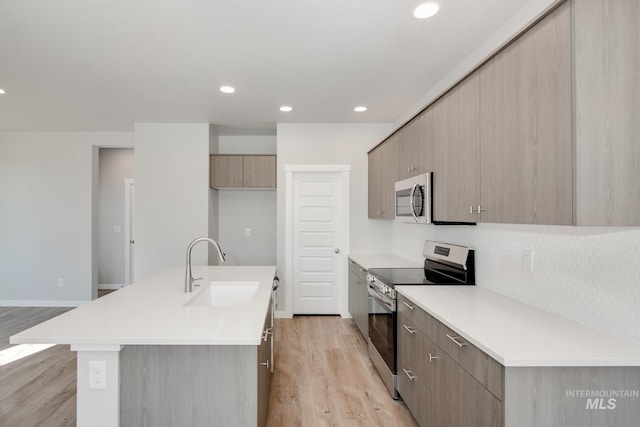 kitchen featuring sink, light hardwood / wood-style flooring, decorative backsplash, an island with sink, and stainless steel appliances