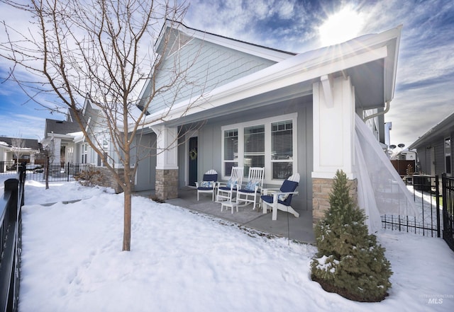 snow covered rear of property featuring board and batten siding, a porch, fence, and stone siding