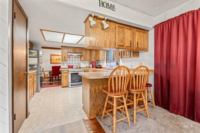 4 N 100 W, Fairfield, ID 83327 - kitchen with appliances with stainless steel finishes, under cabinet range hood, a peninsula, brown cabinetry, and light countertops