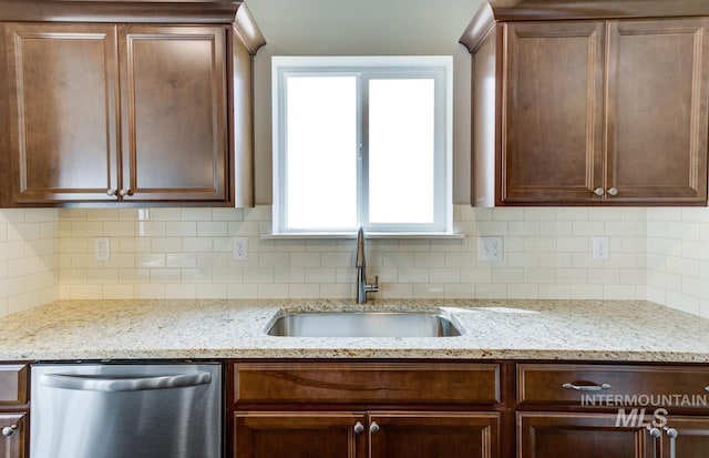 kitchen featuring backsplash, light stone countertops, sink, and stainless steel dishwasher