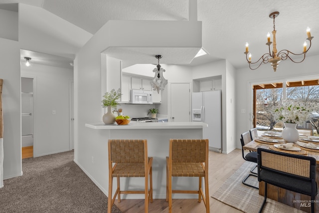 kitchen with white appliances, a breakfast bar, an inviting chandelier, hanging light fixtures, and kitchen peninsula