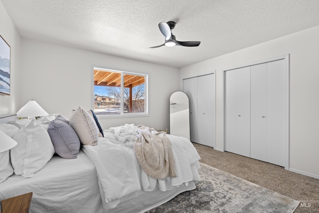 carpeted bedroom with ceiling fan, a textured ceiling, and two closets