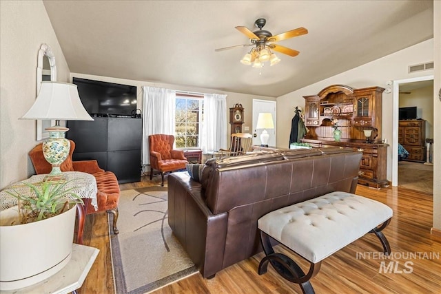 living room featuring lofted ceiling, ceiling fan, visible vents, and light wood-style floors