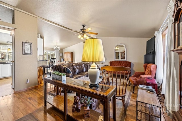 living area with vaulted ceiling, a textured ceiling, ceiling fan with notable chandelier, and wood finished floors