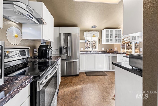 kitchen with stainless steel appliances, range hood, dark countertops, and a textured ceiling