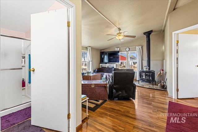 office space with lofted ceiling, a wood stove, ceiling fan, a textured ceiling, and wood finished floors