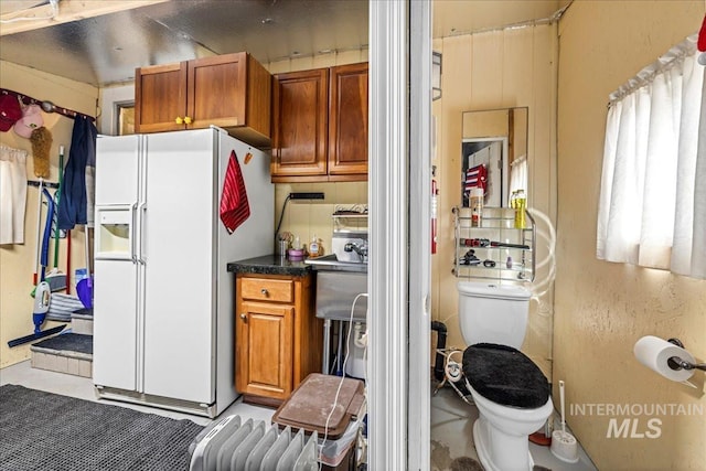 kitchen with white refrigerator with ice dispenser, brown cabinetry, and dark countertops