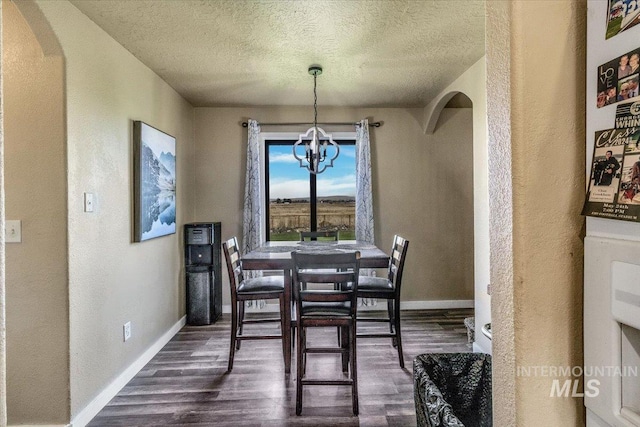 3976 Ranch Ln, Emmett, ID 83617 - dining room featuring arched walkways, a textured wall, baseboards, a notable chandelier, and dark wood-type flooring