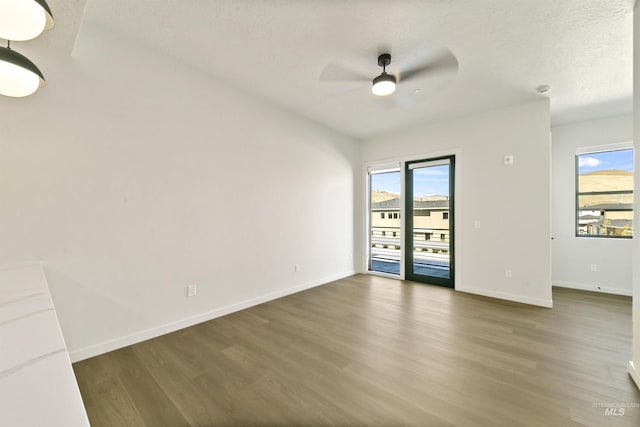 empty room featuring baseboards, a ceiling fan, wood finished floors, and a healthy amount of sunlight