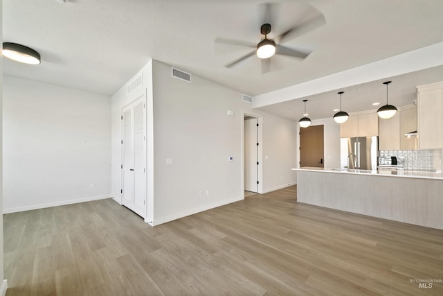 unfurnished living room with visible vents, light wood-style flooring, ceiling fan, and baseboards