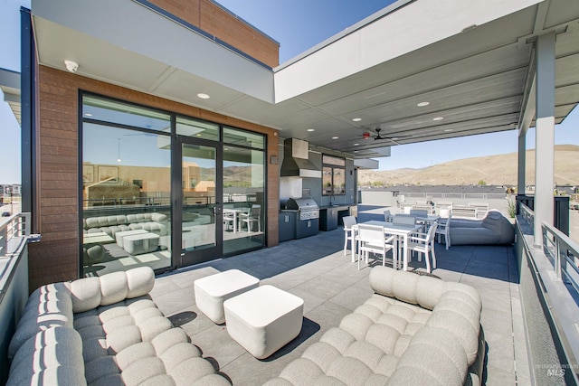 view of patio / terrace with grilling area, a ceiling fan, outdoor dining area, a mountain view, and an outdoor kitchen