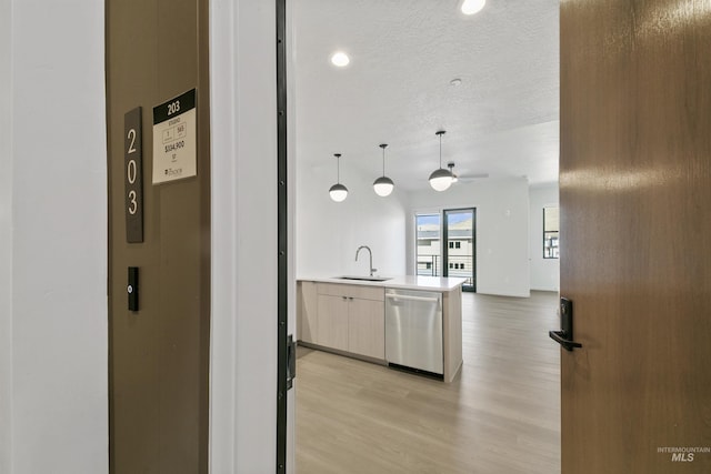 kitchen with stainless steel dishwasher, a sink, open floor plan, and light wood-type flooring