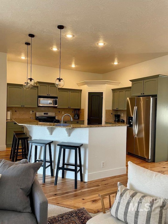 kitchen with decorative light fixtures, appliances with stainless steel finishes, a kitchen breakfast bar, green cabinets, and stone counters