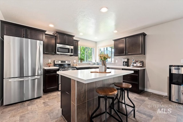 kitchen with stainless steel appliances, a kitchen breakfast bar, light countertops, backsplash, and a kitchen island