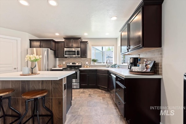 kitchen featuring stainless steel appliances, a breakfast bar area, tasteful backsplash, light countertops, and stone finish floors