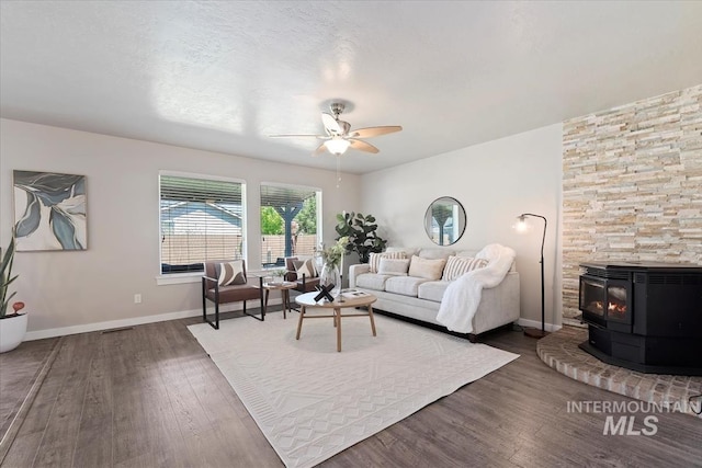 living room with wood finished floors, a wood stove, ceiling fan, and baseboards