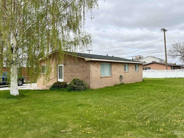 view of property exterior with a yard, brick siding, and fence