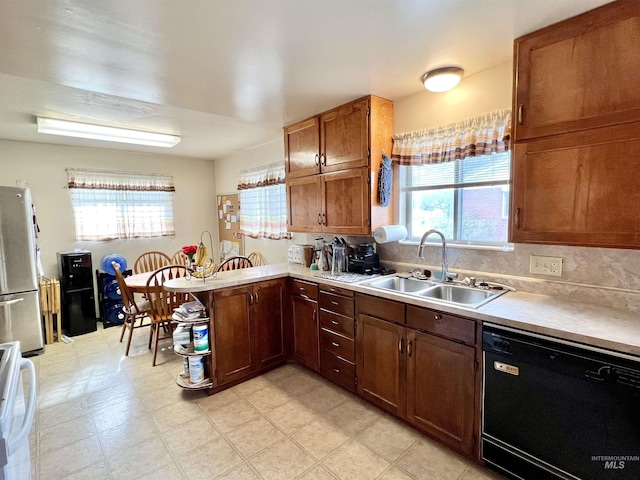 kitchen with freestanding refrigerator, a peninsula, light countertops, a sink, and dishwasher