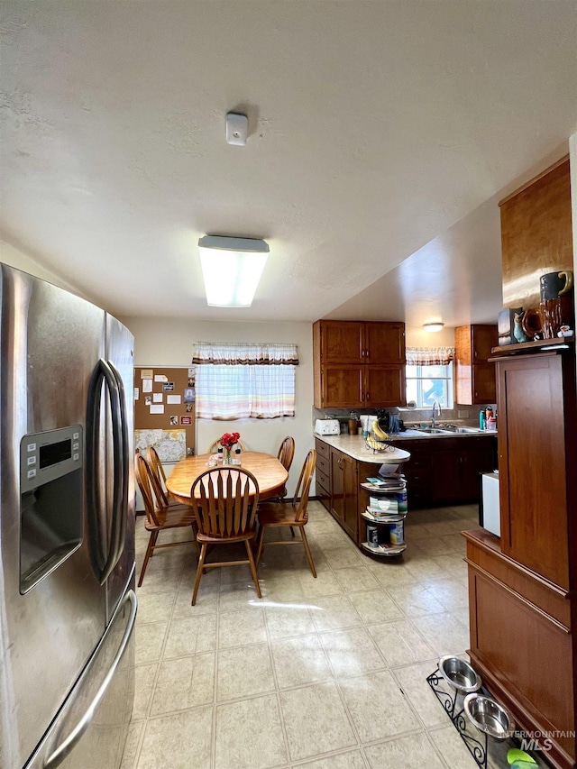 kitchen featuring a sink, brown cabinetry, and stainless steel refrigerator with ice dispenser