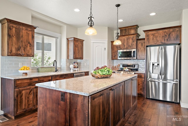 kitchen with a textured ceiling, a kitchen island, dark hardwood / wood-style flooring, appliances with stainless steel finishes, and hanging light fixtures