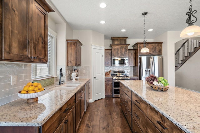 kitchen with light stone counters, a center island, dark wood-type flooring, hanging light fixtures, and appliances with stainless steel finishes