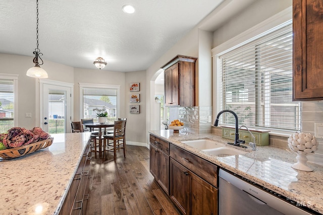 kitchen with dark hardwood / wood-style floors, dishwasher, hanging light fixtures, sink, and light stone counters