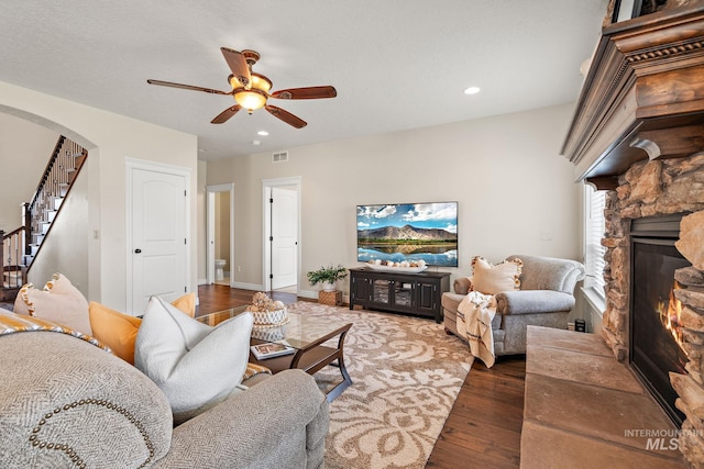 living room with a fireplace, dark wood-type flooring, and ceiling fan