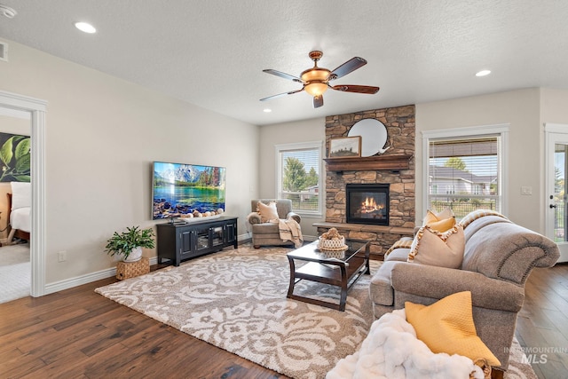 living room with a textured ceiling, ceiling fan, dark hardwood / wood-style floors, and a stone fireplace