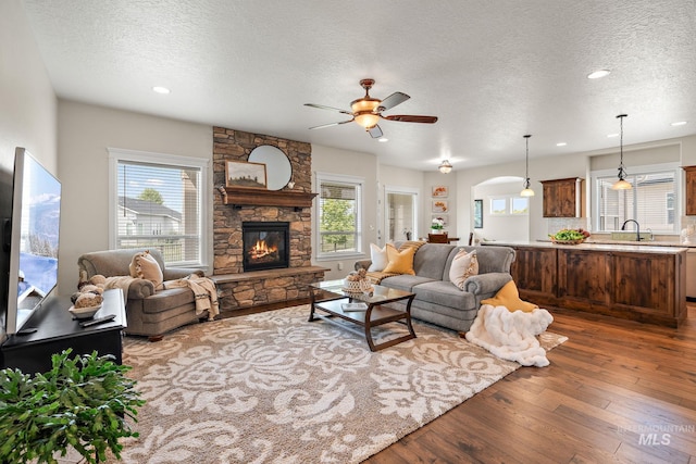 living room with a textured ceiling, dark hardwood / wood-style flooring, a fireplace, sink, and ceiling fan