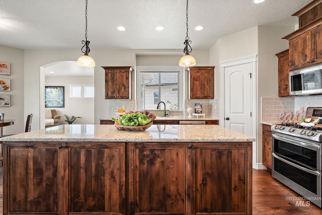 kitchen featuring appliances with stainless steel finishes, light stone countertops, tasteful backsplash, and hanging light fixtures