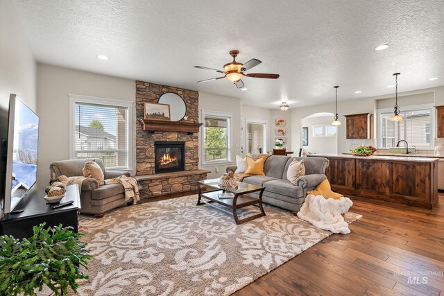 1175 N Champions Pl, Eagle, ID 83616 - living room with a stone fireplace, a ceiling fan, dark wood-style floors, and a textured ceiling