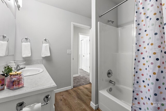 full bathroom with wood finished floors, shower / bathtub combination with curtain, vanity, and baseboards